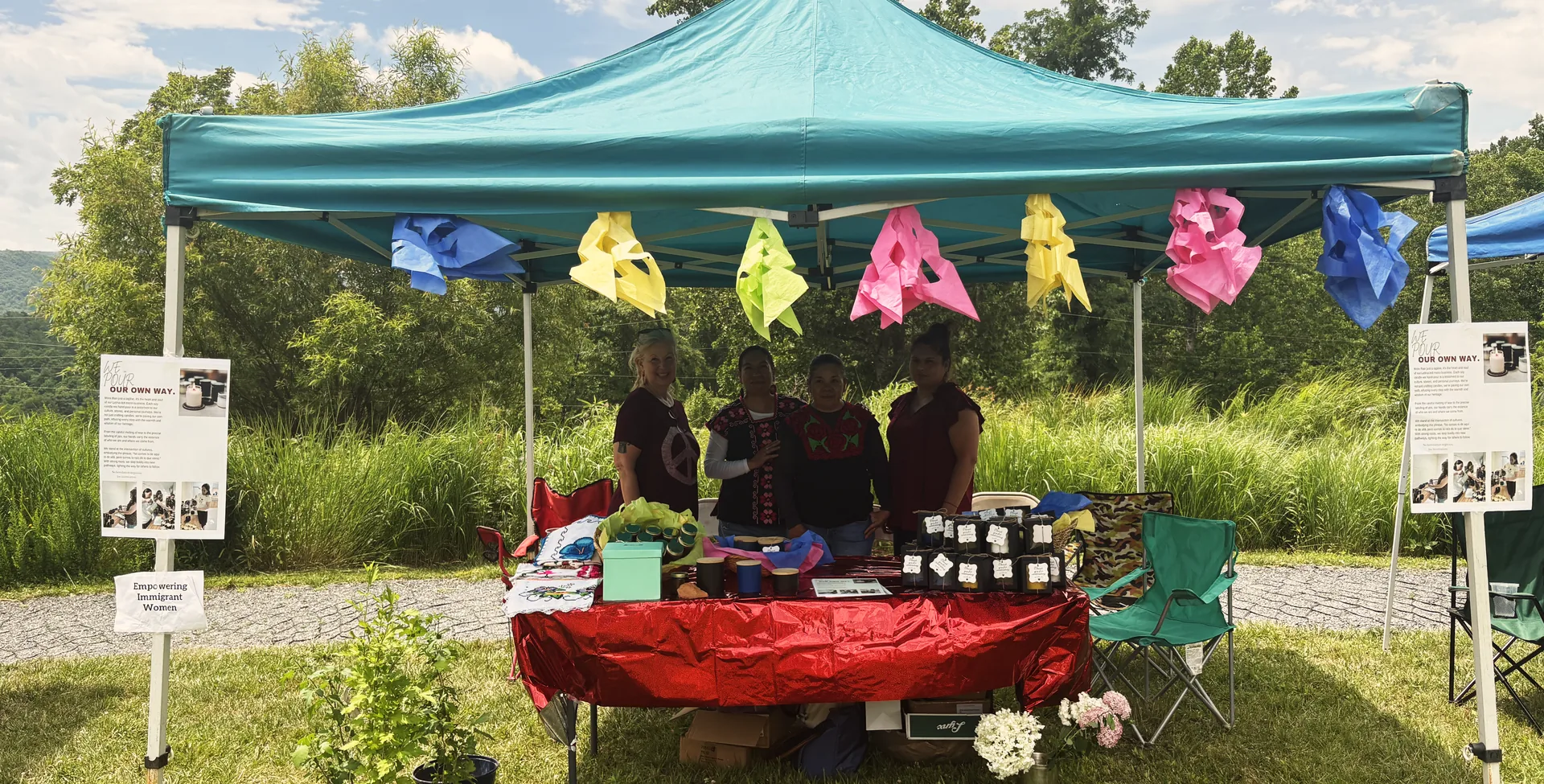 The women of Las Adelitas at their booth at a local Western North Carolina market, with the Blue Ridge mountains behind them